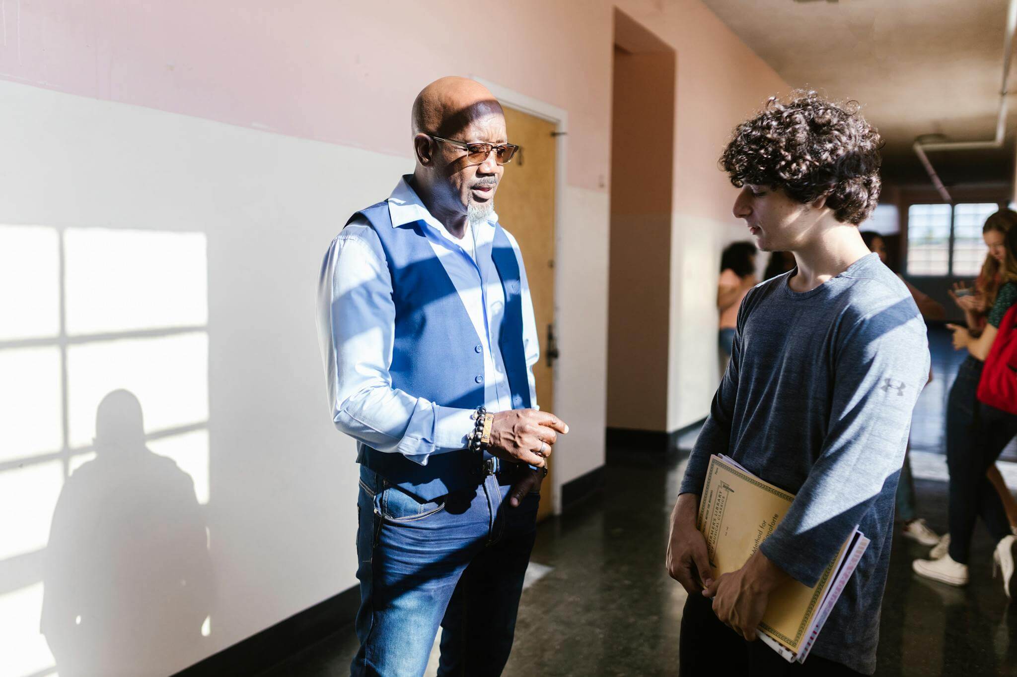 A teacher and student engaging in discussion in a school hallway.