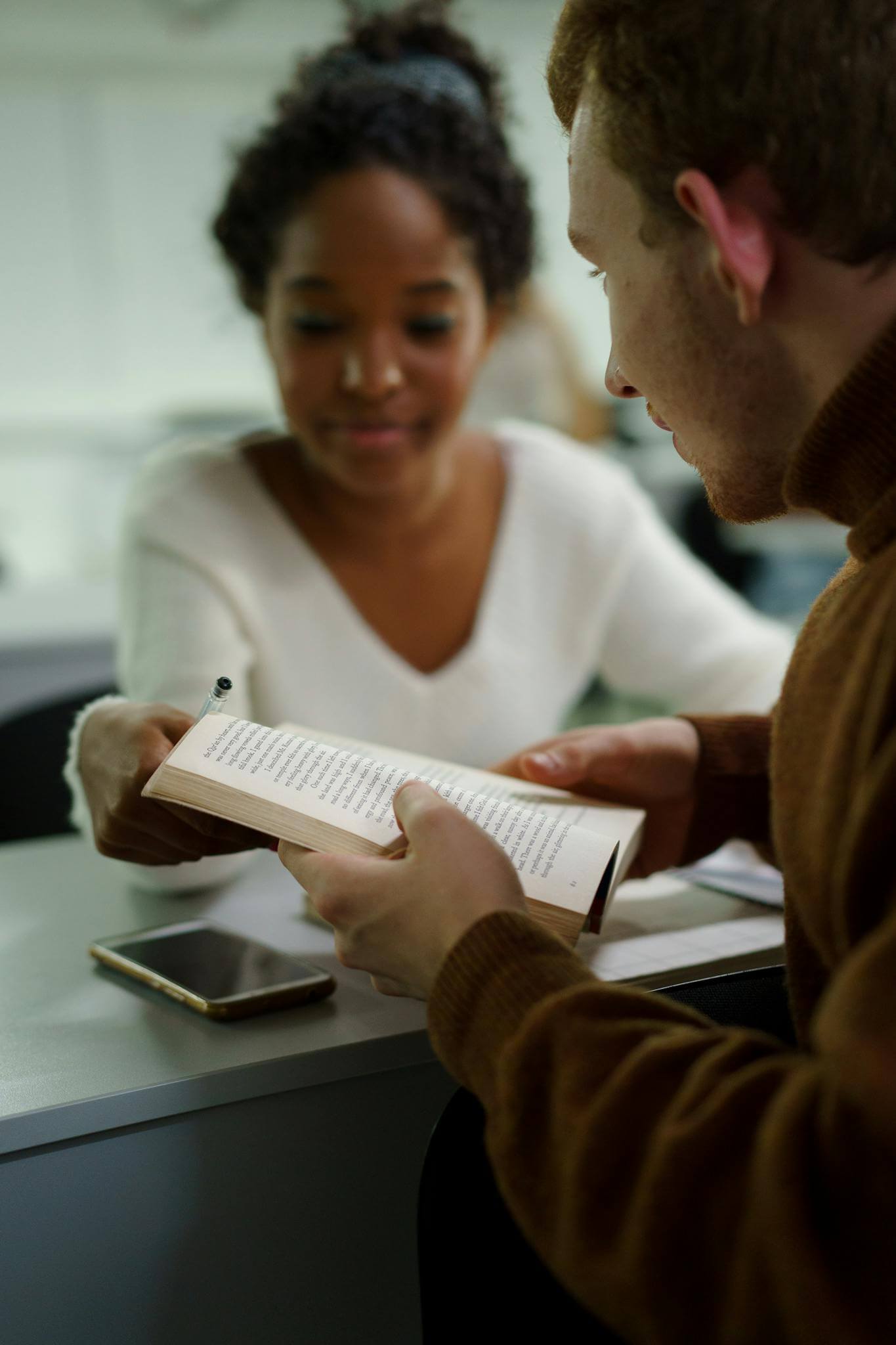 Two university students engaged in studying together, sharing a book and notes.